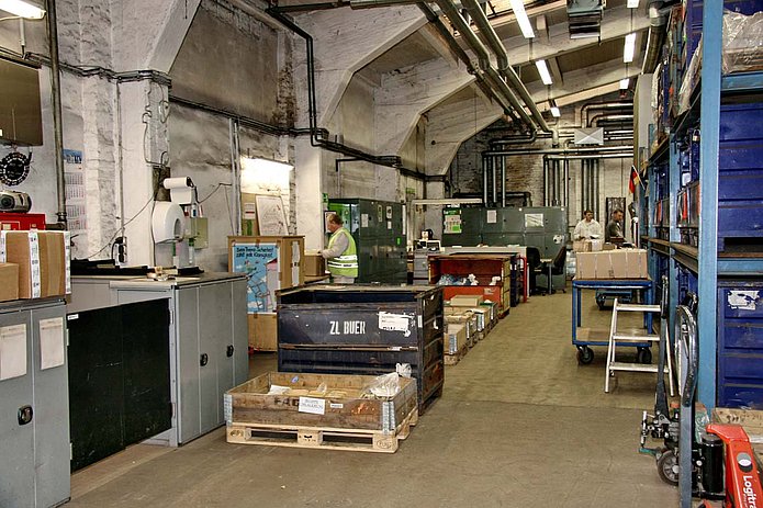 Regallager Innenansicht, gefüllte Regale in einer Halle, drei Männer verpacken Materialien 