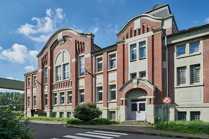 Frontansicht der Lohn-Lichthalle: Rotes Backsteingebäude, davor eine Straße und etwas Grünfläche.