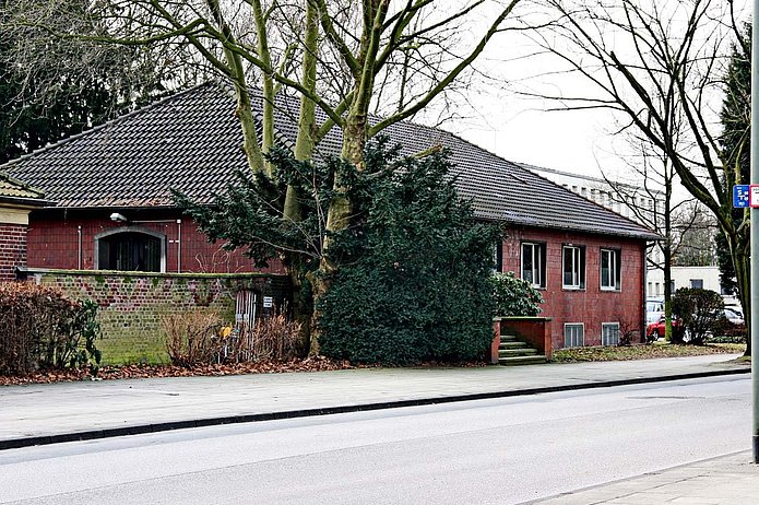 Gesundheitshaus Außenansicht, rotes Backsteinhaus, verdeckt von Baum und Busch