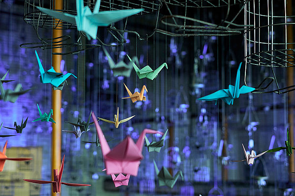 Neonfarbene Origami-Kraniche leuchten als Lichtinstallation, aufgehängt an Kauenkörben in der Schwarzkaue
