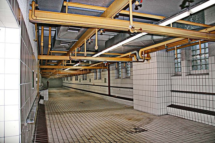 Waschkaue Innenansicht, voll weiß gefliester Raum mit Kupferrohren an der Decke