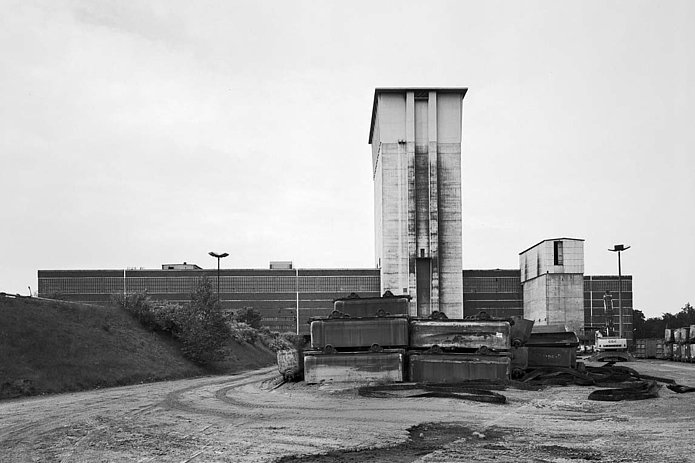 Schacht 3 Außenansicht, ein großer Turm mit Gebäude im Hintergrund und Containern im Vordergrund, historische schwarz-weiß Aufnahme