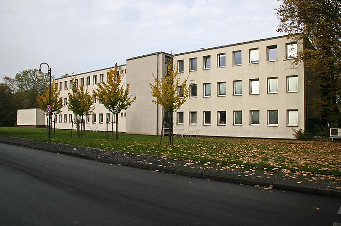 Verwaltungsgebäude Außenansicht, längliches weißes Gebäude mit Begrünung davor