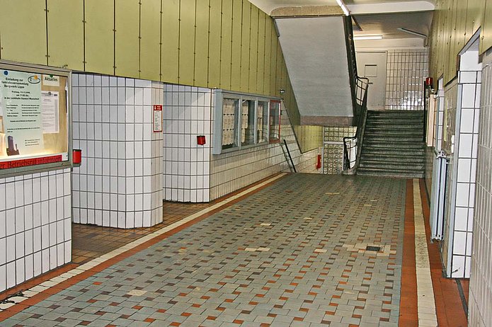 Lohn-& Lichthalle Innenansicht, ein Flur mit Treppenaufgang, die Wände sind weiß gefliest und der Boden grün-orange