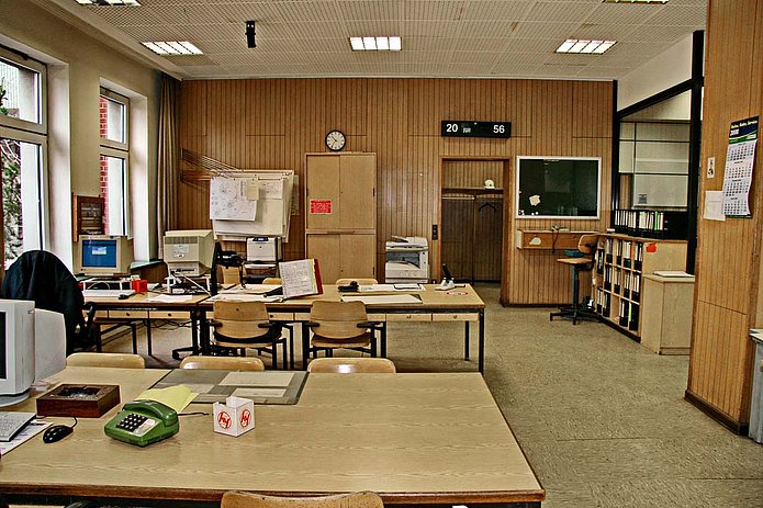 Lohn-& Lichthalle Innenansicht, Büroraum mit Holzverkleidung, Holztischen und -stühlen, auf den Tischen stehen weiße, alte Bildschirme für Computer