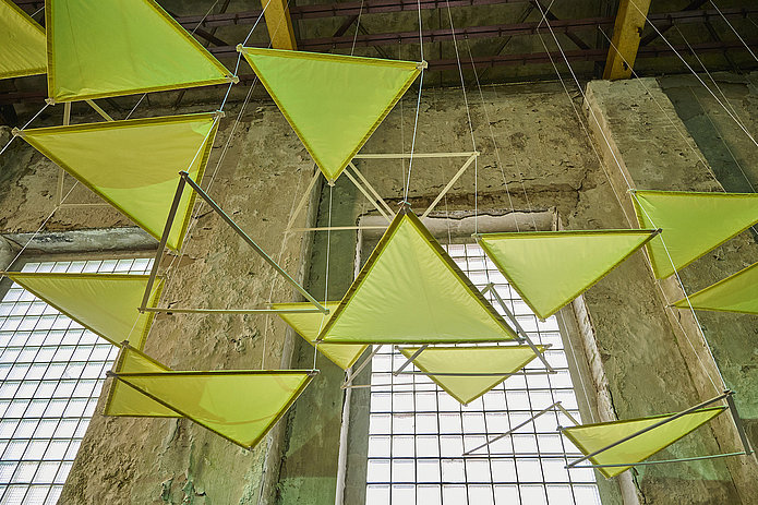 Blick von unten auf eine Deckeninstallation aus neonfarbenen Dreiecken.