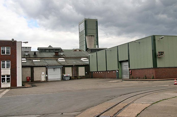 Lagerhalle Außenansicht, grüne Blechverkleidung und ein graues Rolltor mit anliegenden Gebäuden